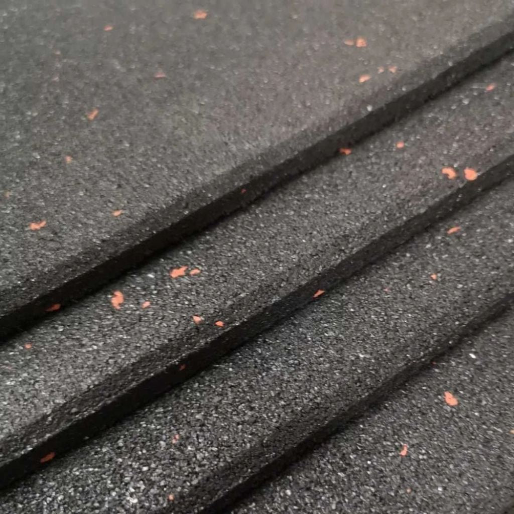 A stacked pile of heavy-duty black rubber gym floor tiles with red speckles, showing their durable thickness and slip-resistant flecked design.