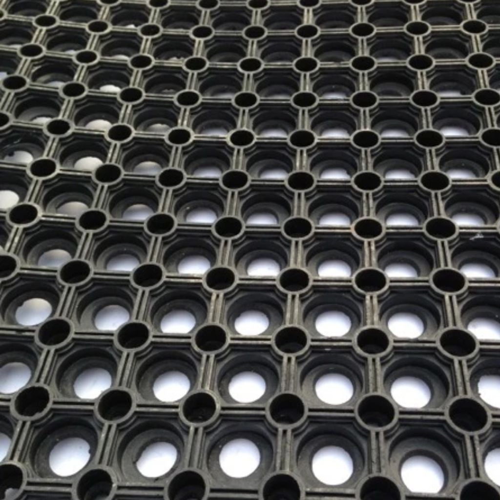 A close-up view of a black plastic grid mat with a repeating honeycomb pattern of circular holes.