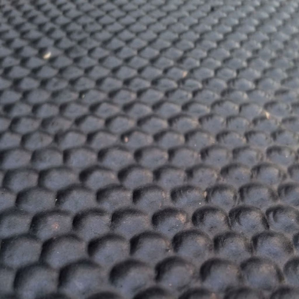Close-up of a dark gray textured surface with a repeating raised circular bubble or honeycomb-like pattern.