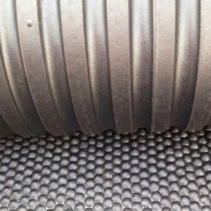 Close-up of a dark gray ribbed corrugated pipe resting on a black honeycomb-patterned textured surface.