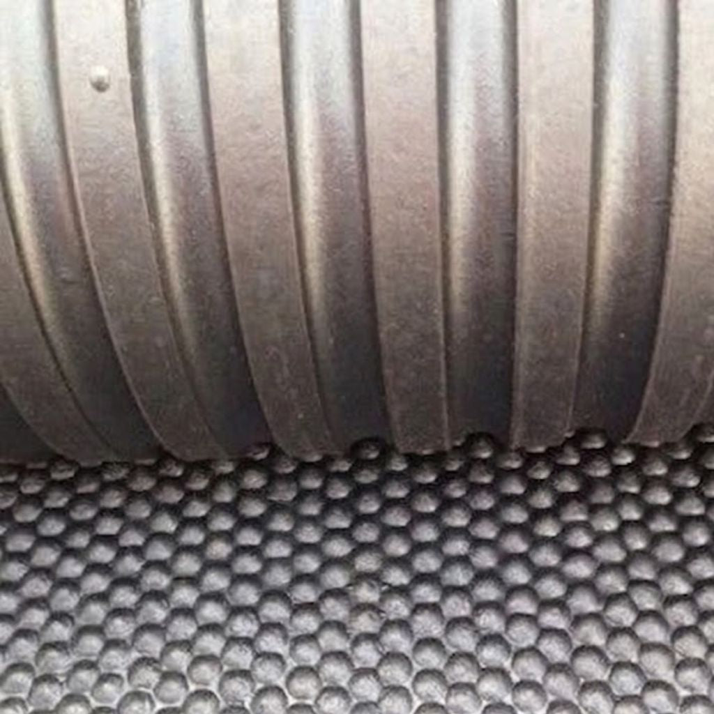 Close-up of a dark gray ribbed corrugated pipe resting on a black honeycomb-patterned textured surface.