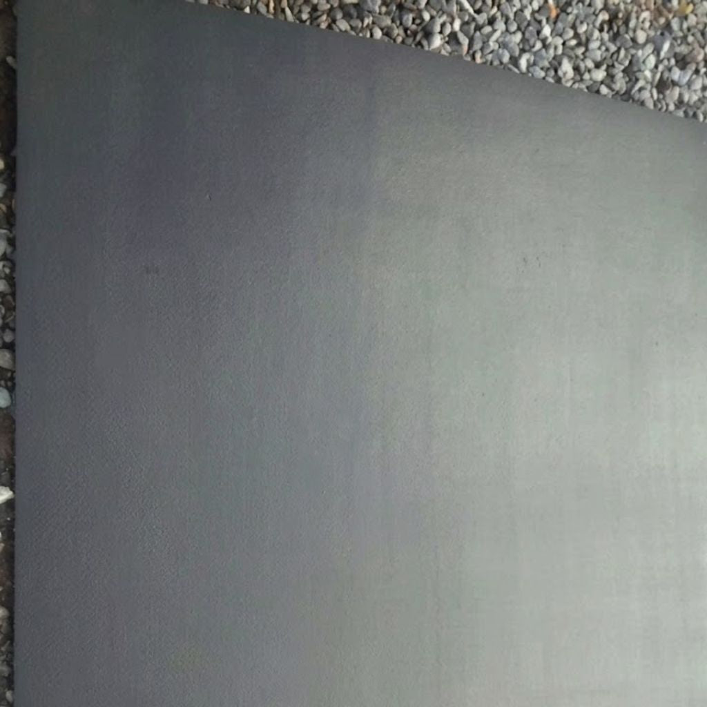 A large, flat rectangular dark gray panel or sheet of material shown from above, with gravel visible along the top and left edges.