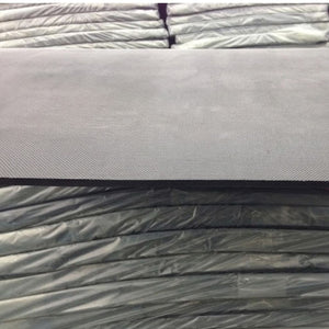 A close-up of a dark gray textured fabric or material sample resting on top of stacked similar material rolls wrapped in plastic.