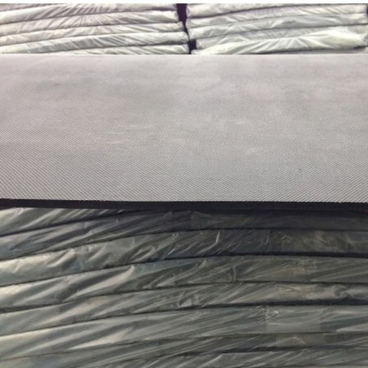 A close-up of a dark gray textured fabric or material sample resting on top of stacked similar material rolls wrapped in plastic.
