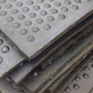 A close-up stack of dark gray perforated metal plates with circular holes, showing the textured surface and layered edges.