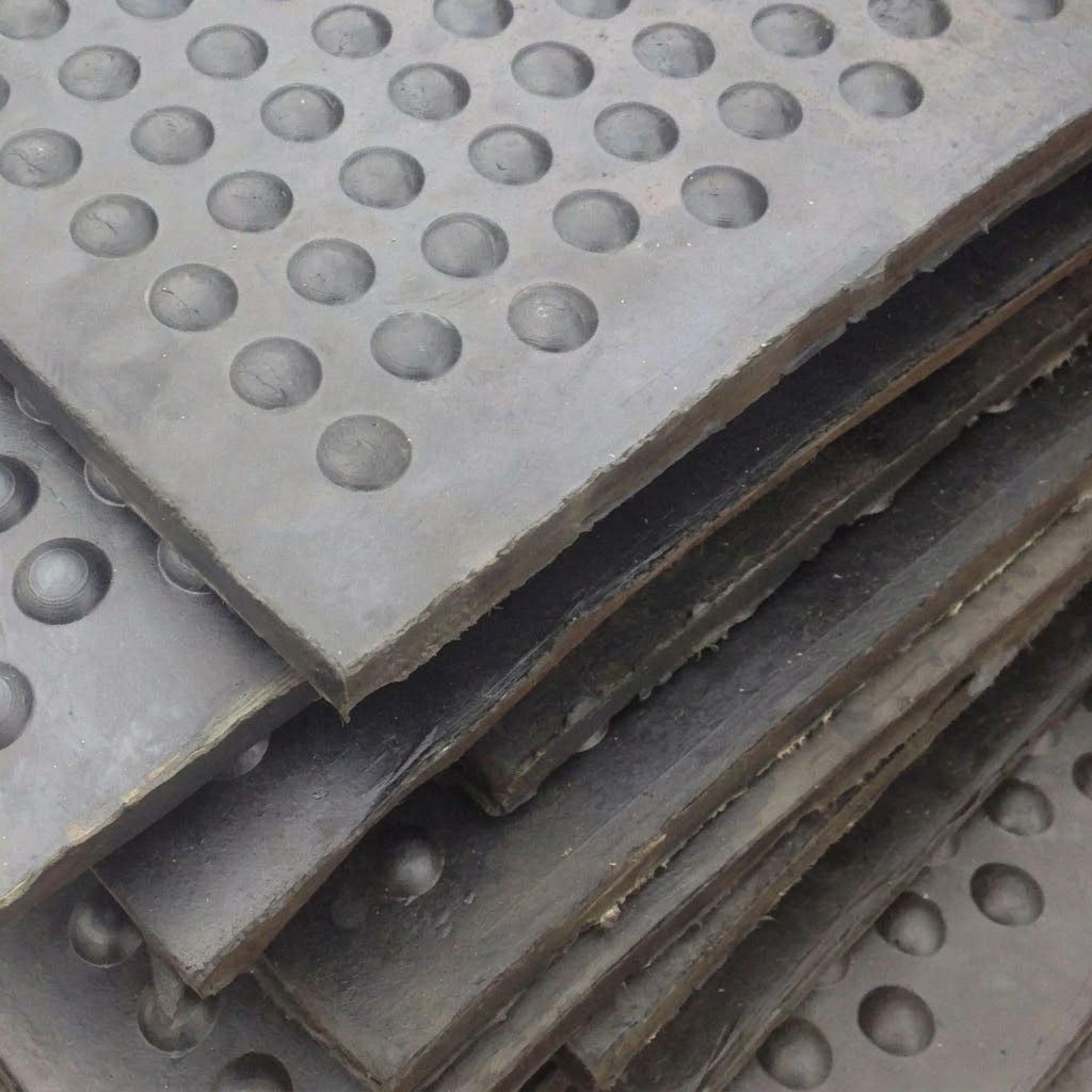 A close-up stack of dark gray perforated metal plates with circular holes, showing the textured surface and layered edges.