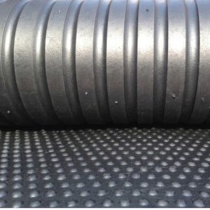 Close-up of a black ribbed corrugated tube resting on a textured black mat with a circular dot pattern.