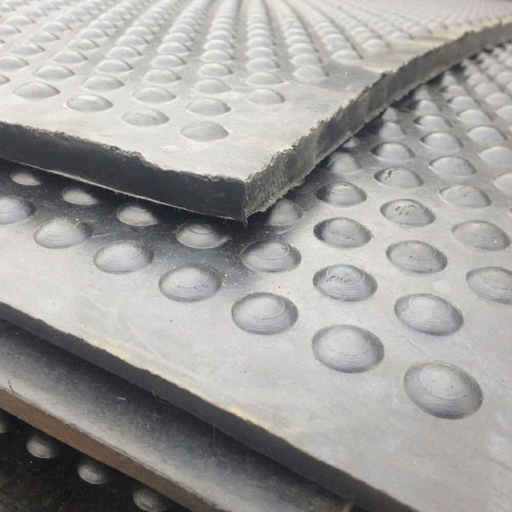 Close-up of stacked gray rubber or foam mats with a raised circular bubble texture, showing the thickness and surface detail of the top layer.