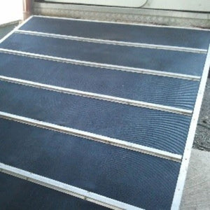 A metal ramp with textured dark gray or black rubber panels between silver metal rails, photographed outdoors.