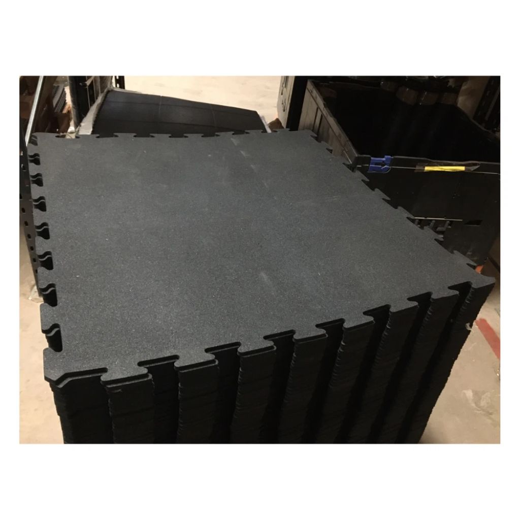 A stack of black interlocking foam floor tiles with a textured surface, photographed in what appears to be a warehouse or storage area.