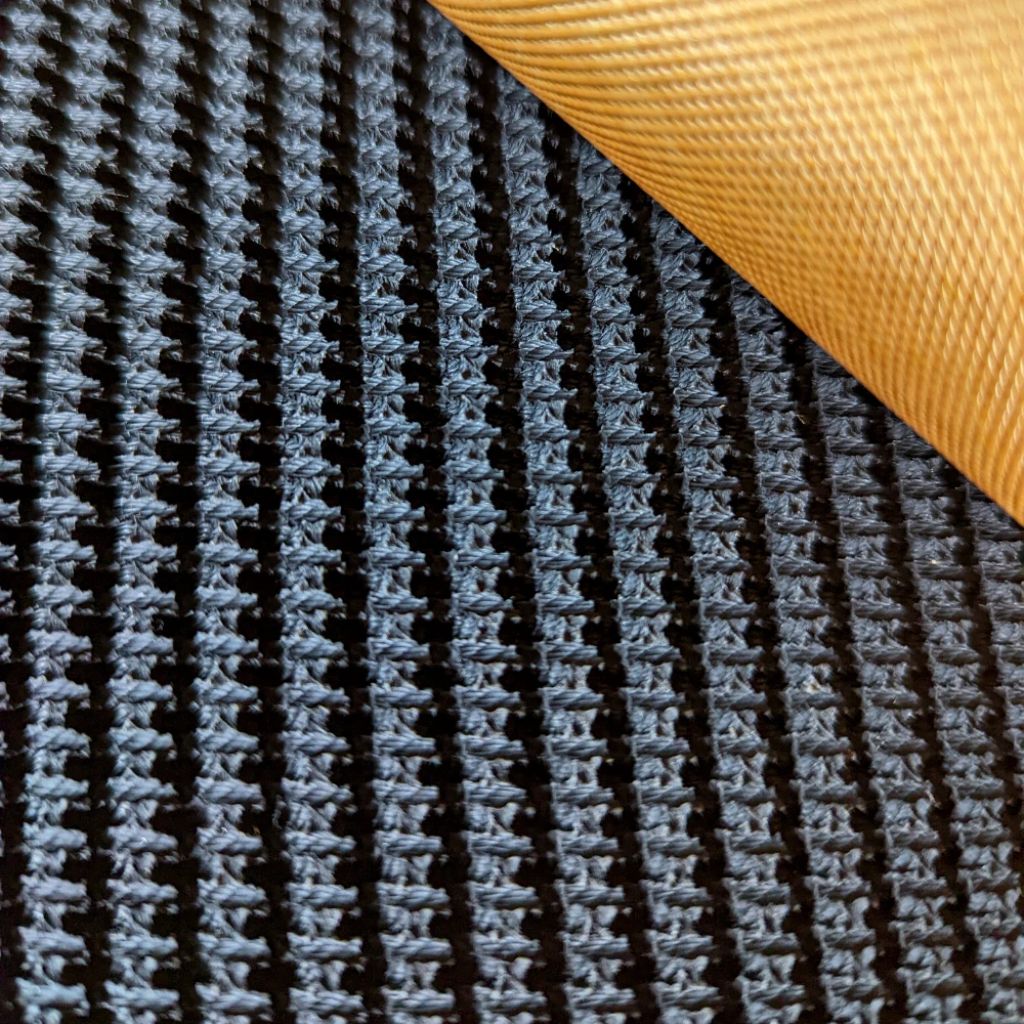 Close-up of a textured black mesh or woven mat with a rolled corner revealing a golden-yellow underside.