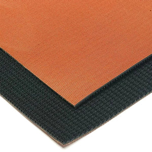 Close-up of a square mat or pad showing two textured surfaces: a warm orange top side and a dark charcoal/black side, photographed on a white background.