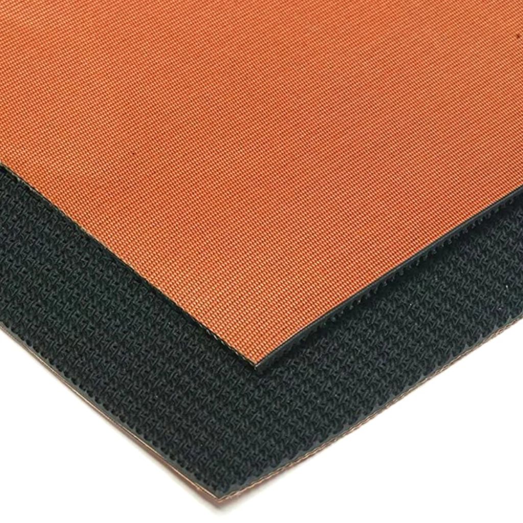 Close-up of a square mat or pad showing two textured surfaces: a warm orange top side and a dark charcoal/black side, photographed on a white background.