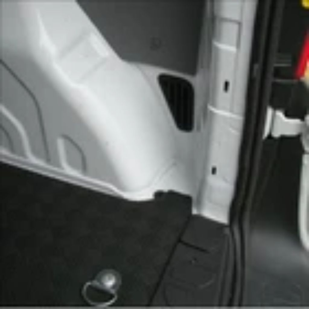 Close-up of the interior side panel and门槛 of a vehicle, showing a white molded plastic side wall, black carpeted floor, and dark trim.