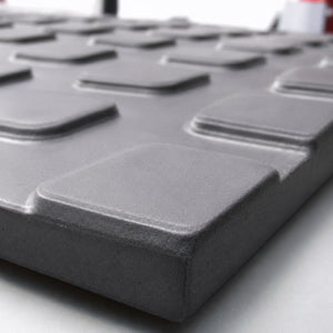 A close-up of a dark gray textured panel with raised square recesses, shown at an angle on a light surface.
