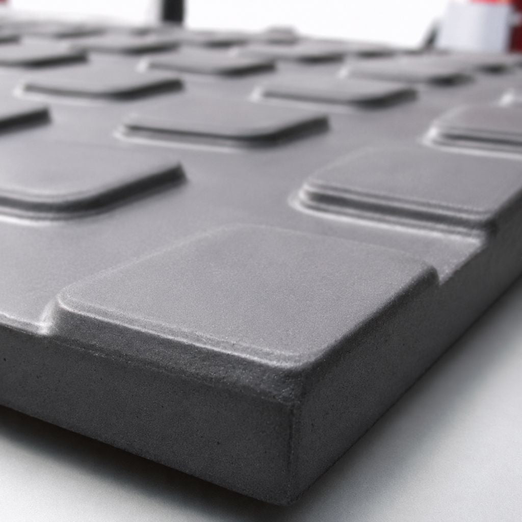 A close-up of a dark gray textured panel with raised square recesses, shown at an angle on a light surface.