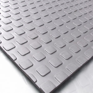 A close-up of a gray textured mat with a repeating raised square pattern, shown at an angle on a white surface.