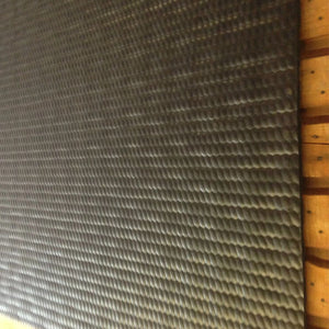 A close-up of a dark gray textured mat with a repeating wavy pattern, shown against a wooden background.