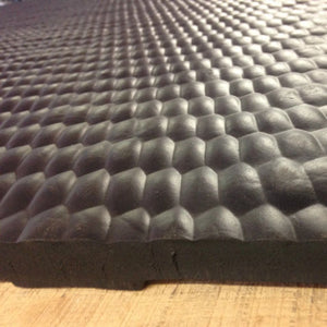 A close-up of a black textured foam mat with a raised honeycomb pattern, resting on a light wood surface.