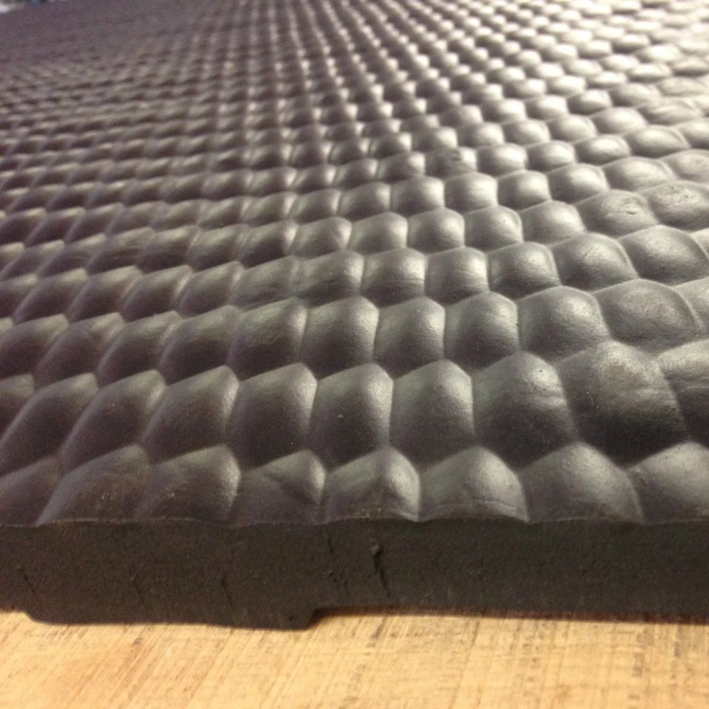 A close-up of a black textured foam mat with a raised honeycomb pattern, resting on a light wood surface.
