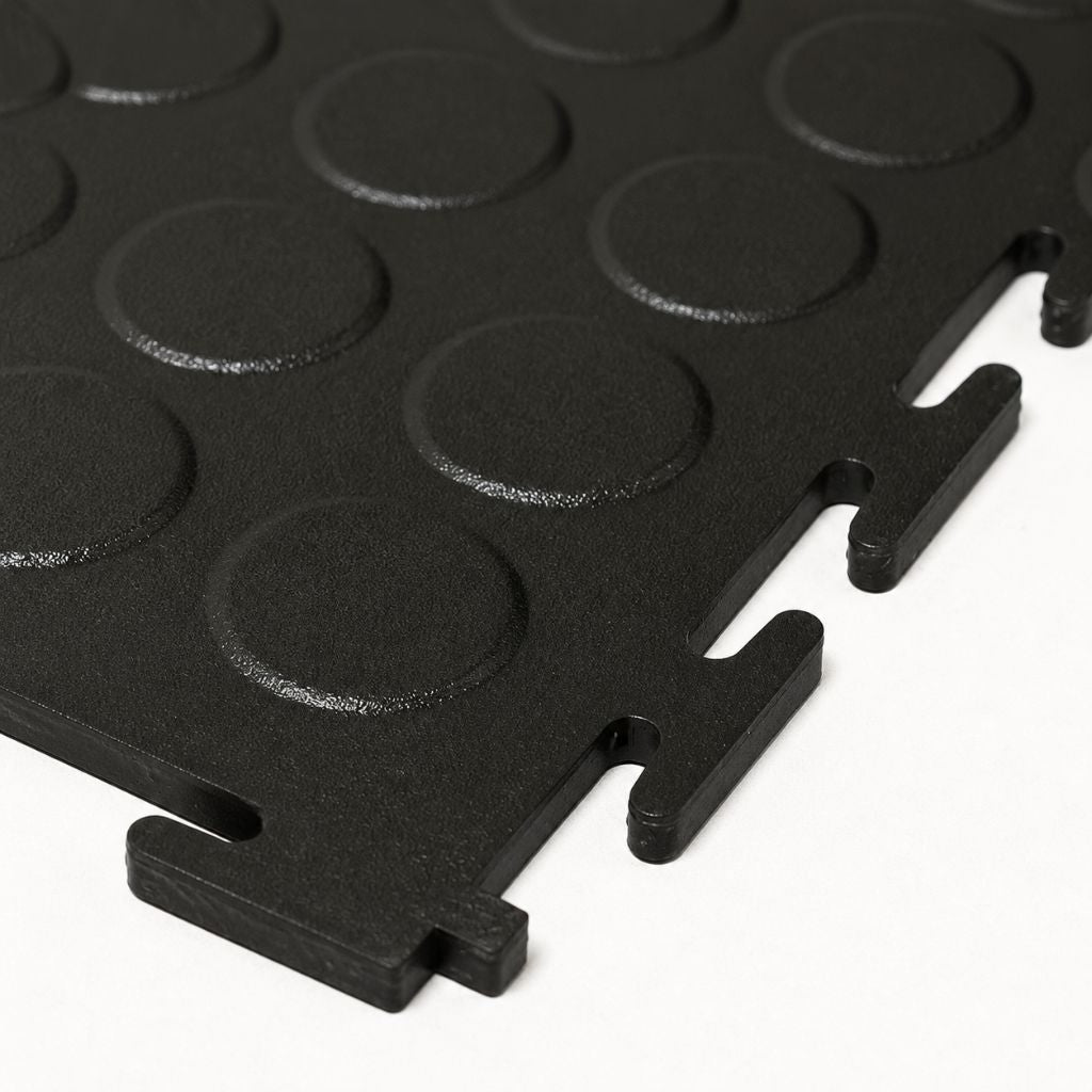 Black interlocking foam floor tiles with circular raised grips and interlocking tabs, shown on a white background.