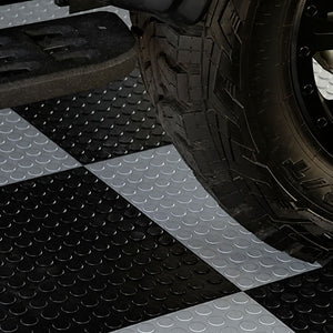 Black and silver checkered rubber floor mats with a raised circular tread pattern, shown under a vehicle tire.
